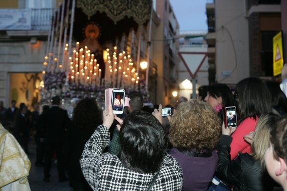 Un grupo de mujeres fotografía el paso de palio de Nuestra Señora de Fe y Caridad por la calle Mariana.