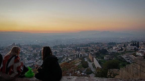 Una pareja, sentada en el Mirador de San Miguel Alto, ante la panorámica de la capital con evidentes signos de contaminación, en una imagen tomada este viernes.  