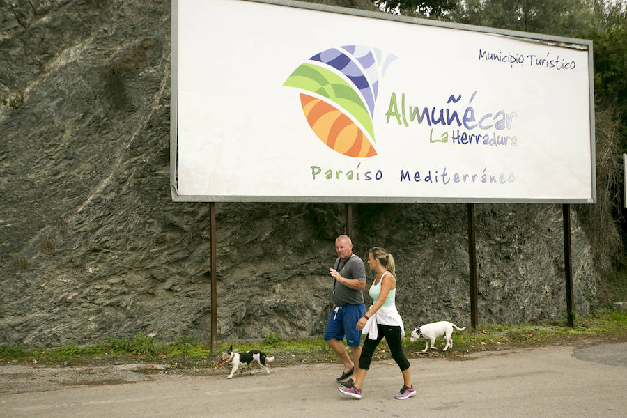 Dos vecinos pasean bajo el cartel de la entrada de Almuñécar en la que luce su título de Municipio Turístico.