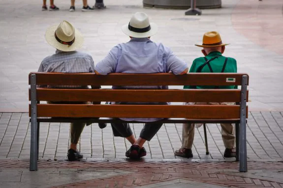 Tres pensionistas descansan en un banco en la calle.