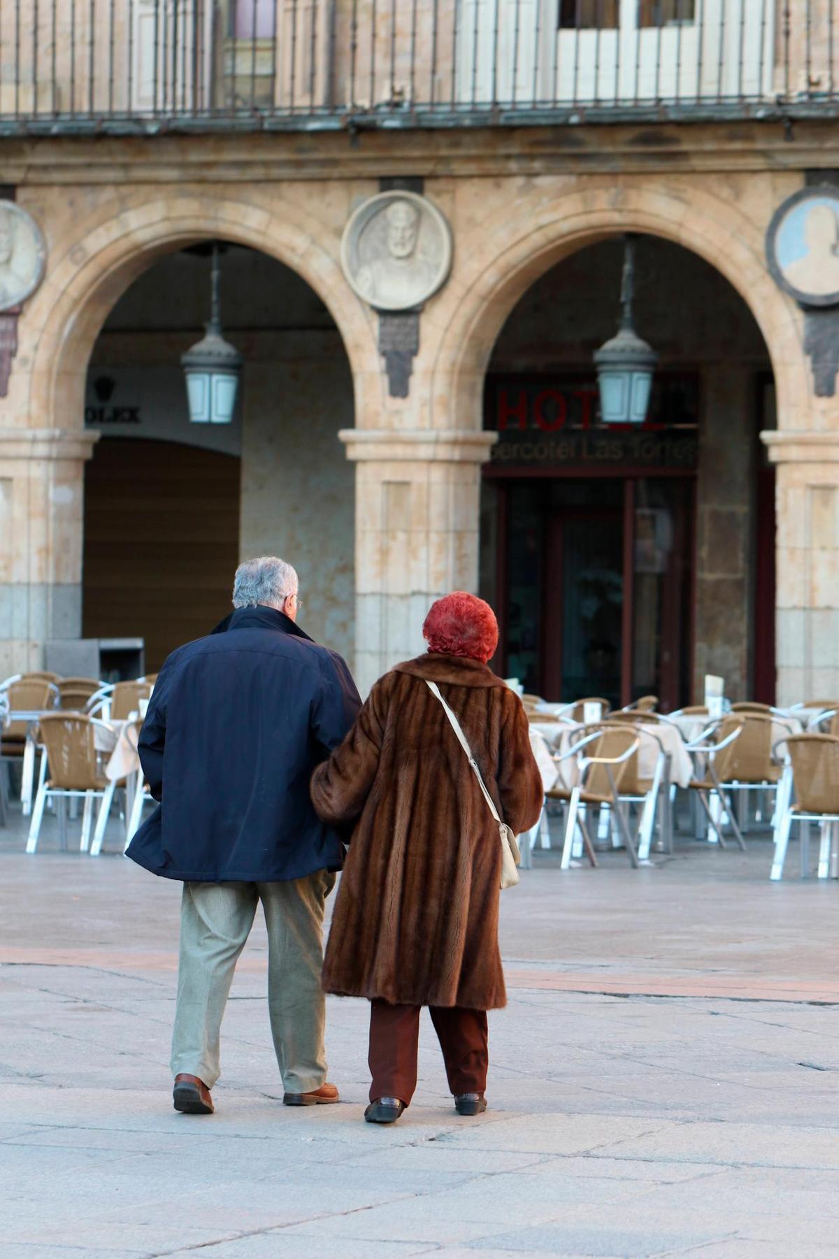 Dos personas mayores pasean por la Plaza Mayor.