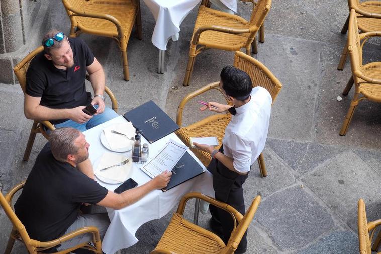 Un camarero atiende a dos clientes en una terraza de la Plaza Mayor.