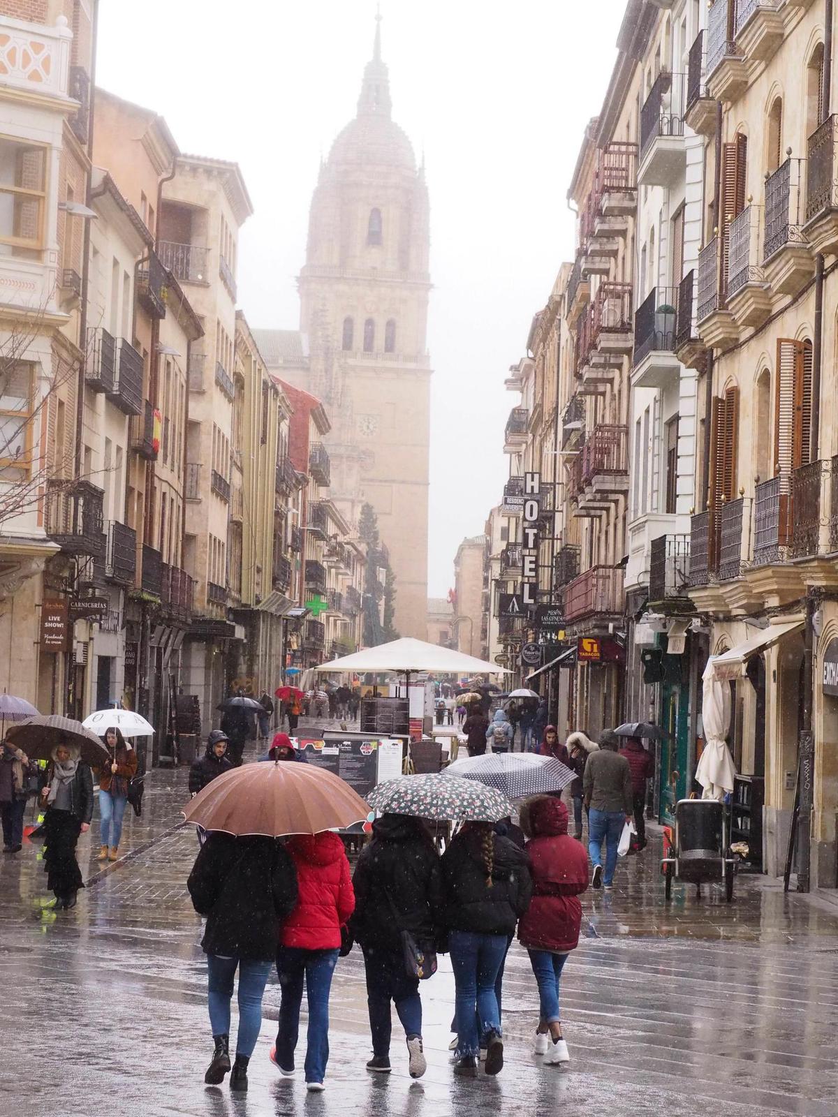 Varias personas pasean por la Rúa con paraguas en un día lluvioso en Salamanca.