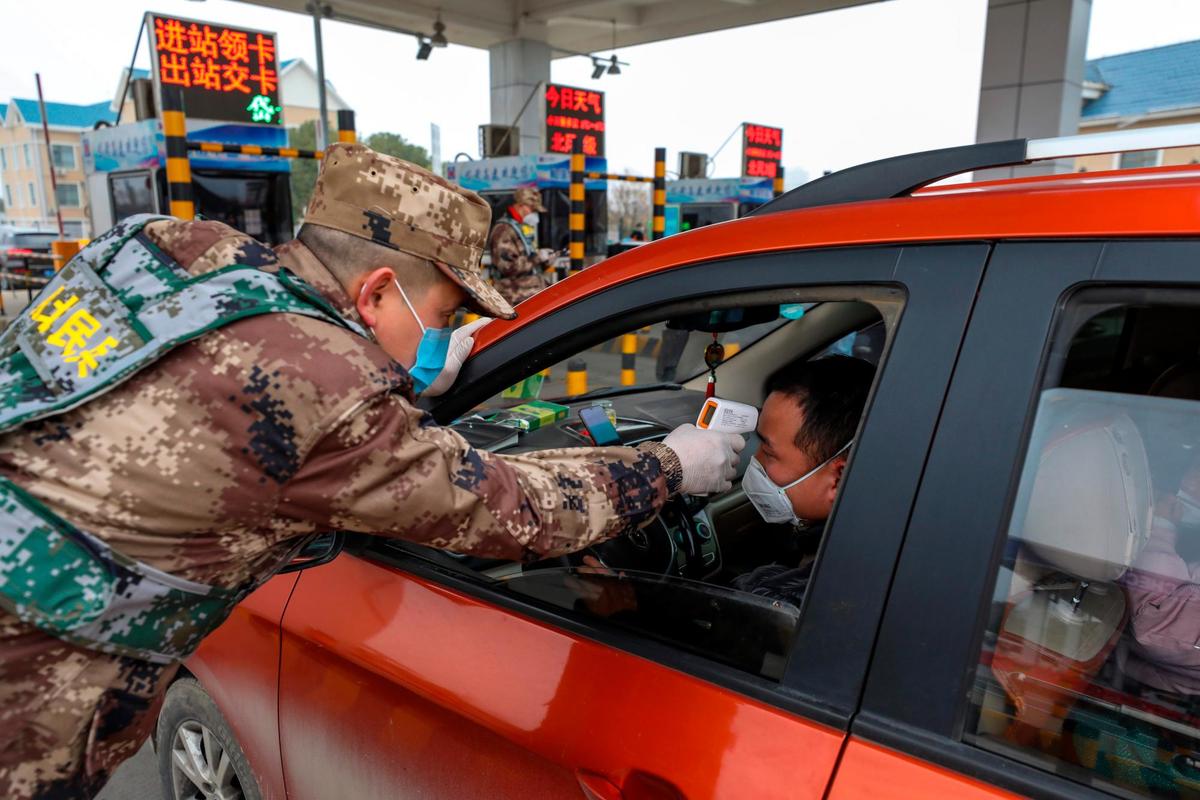 Un soldado mide la fiebre de quienes cruzan la frontera de Wuhan.