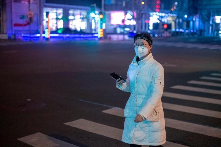 Una muje rpasea por las clales de Shanghai cubriendo su cara con una mascairlla.