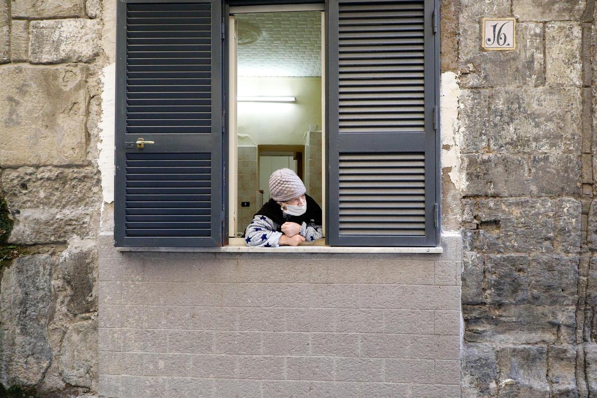 Una mujer con mascarilla en una ventana en Nápoles.