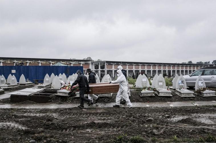 Trabajadores funerarios portan un féretro para enterrarlo en un cementerio en Turín.