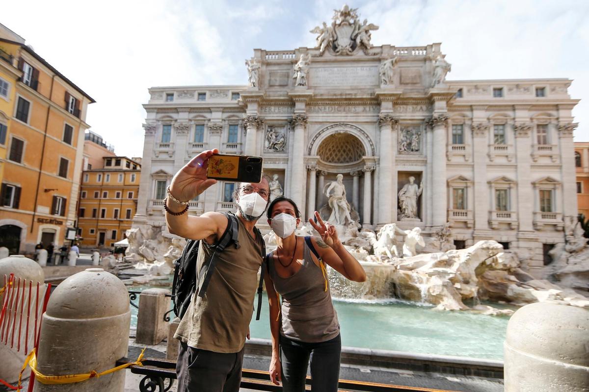 Dos personas con mascarillas se toman una fotografía en la Fontana di Trevi.