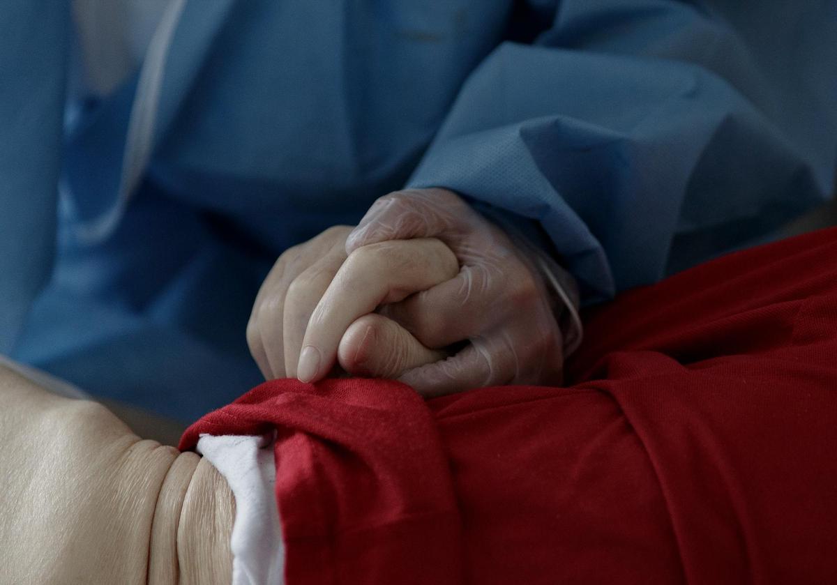 Un sanitario toma la mano de un paciente COVID.