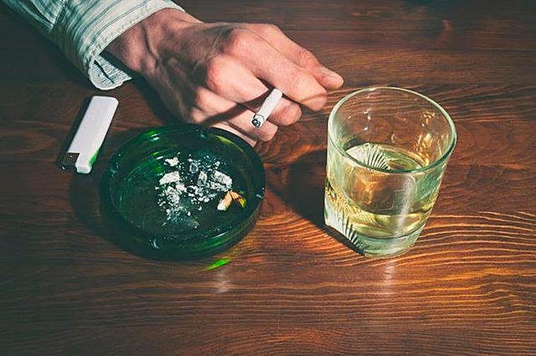 Una personas con un cigarro y una copa de alcohol.
