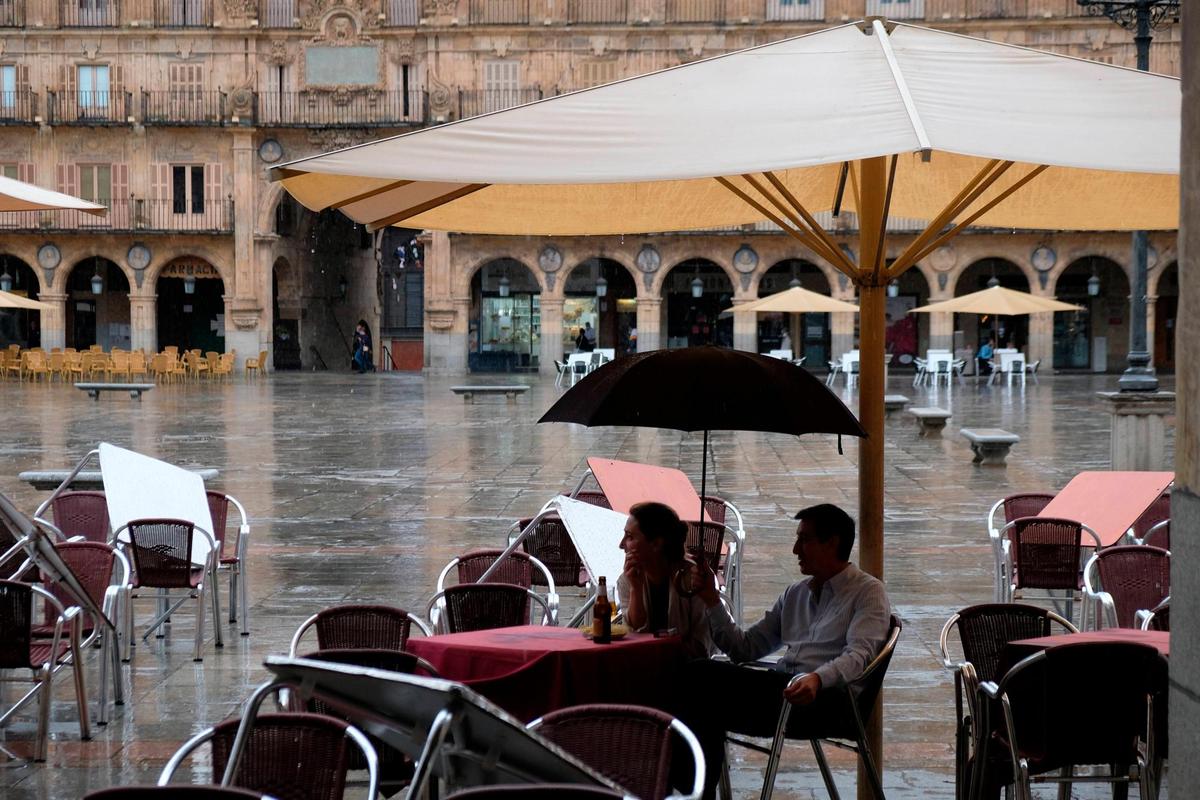 Una pareja se resguarda de la lluvia en la Plaza Mayor