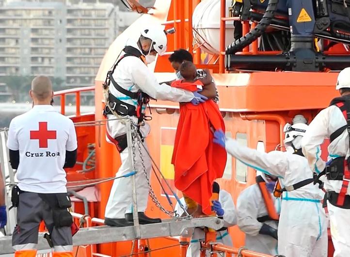 Un miembro de la Cruz Roja ayuda a bajar del barco a una mujer migrante con su niño en el puerto de Arguineguín