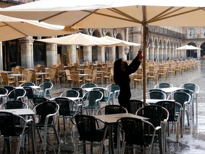 Una camarera ajusta la sombrilla de una terraza.