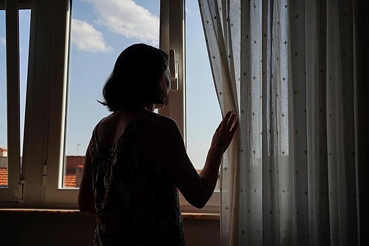 Una joven contempla el exterior desde la ventana de su casa.