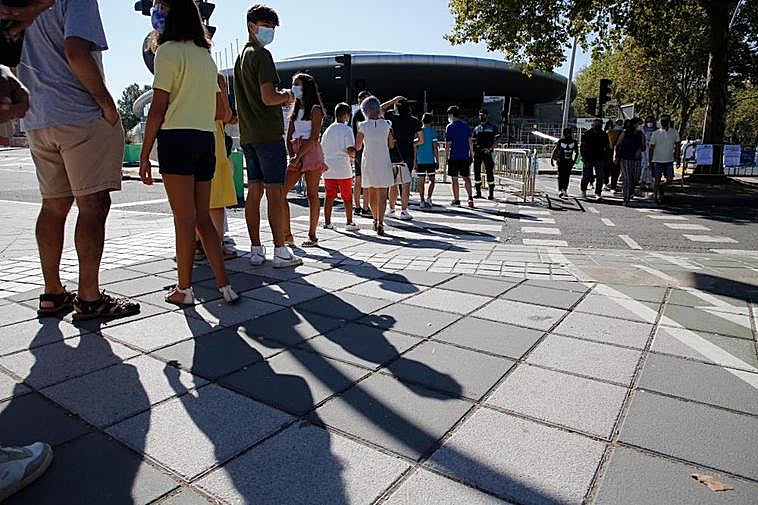 Jóvenes esperan en la cola para entrar a vacunarse en el Multiusos Sánchez Paraíso de la capital.