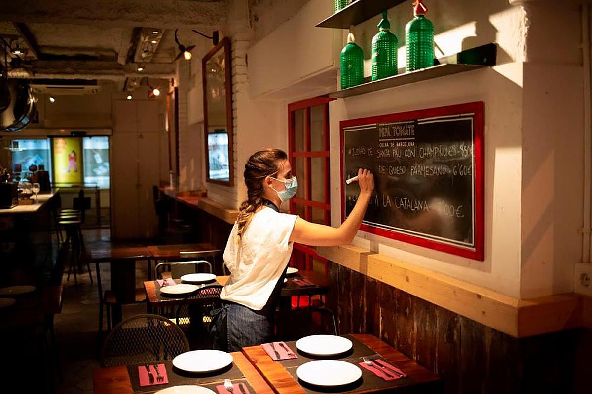 Una camarera apunta platos en una pizarra en el interior de un bar.