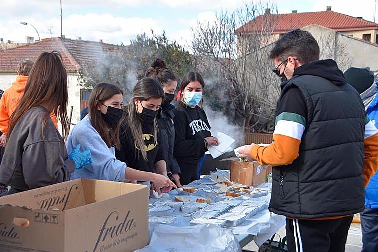 Las peñas y los quintos haciendo el reparto de las raciones solidarias de chichas con huevos