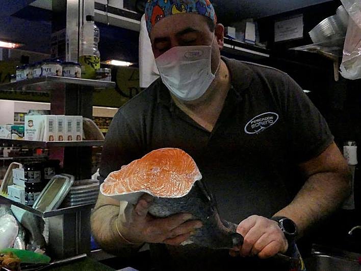 Un pescadero muestra el corte de una pieza de salmón.