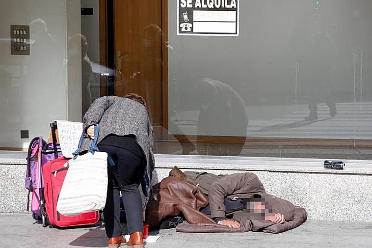 Una mujer deja una moneda junto a un sintecho que duerme en plena calle en la ciudad de Salamanca