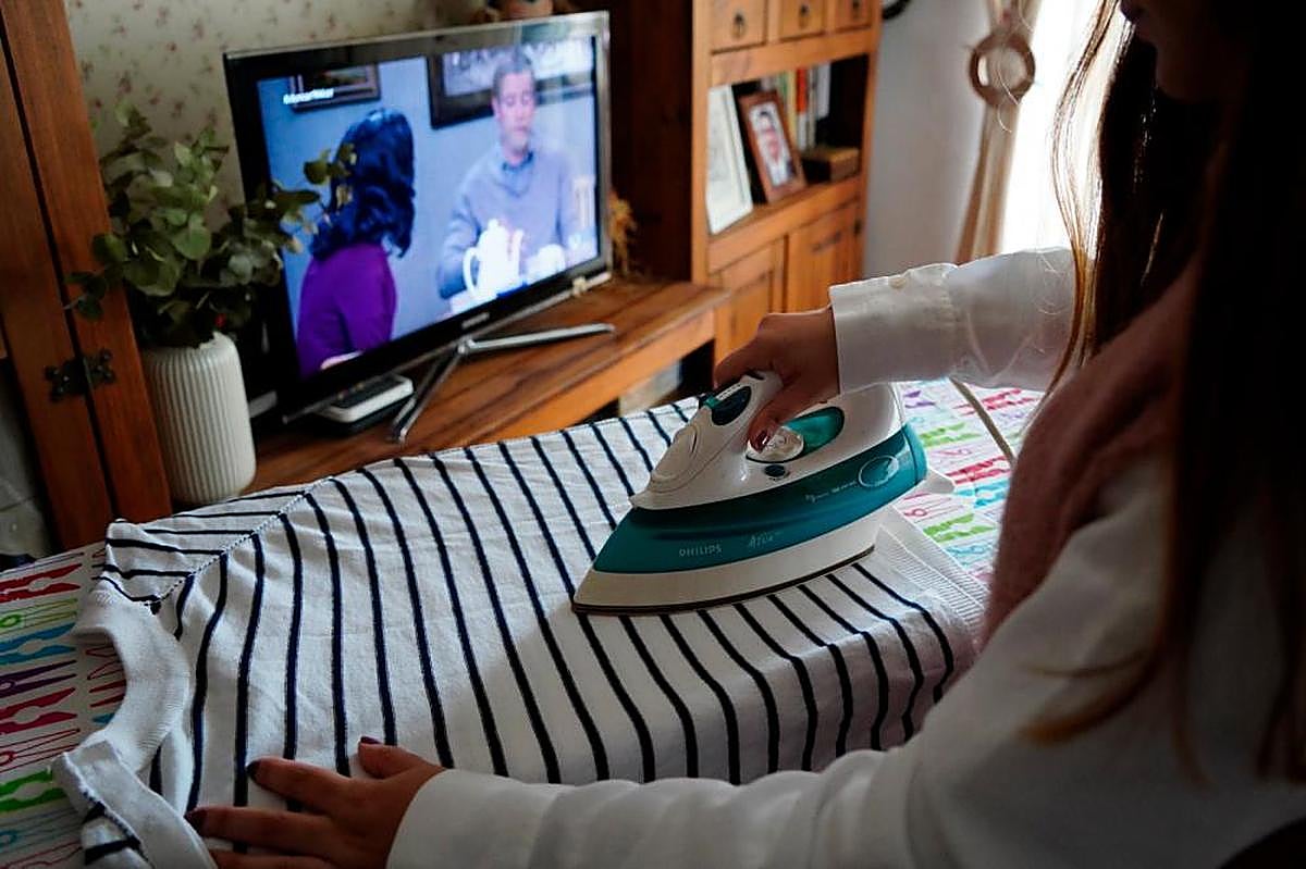 Una mujer plancha mientras ve la televisión en su vivienda de Salamanca.