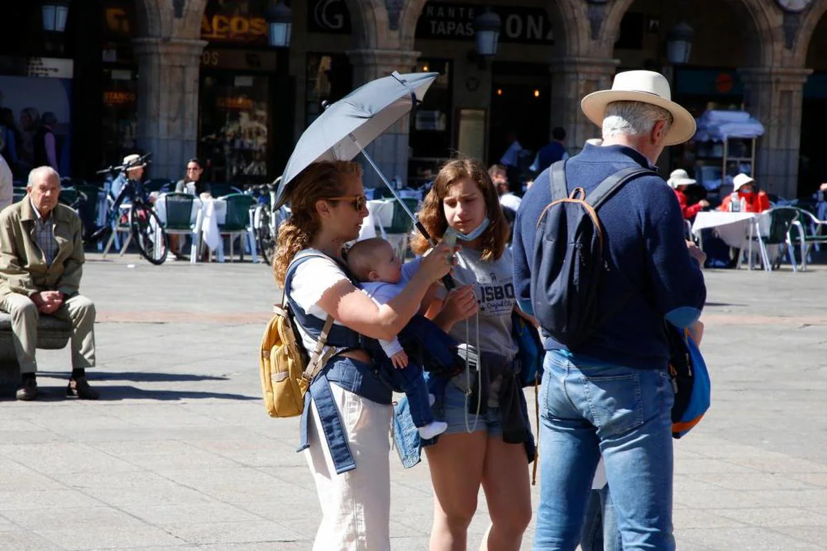 Varias personas se refugian del calor bajo un paraguas.