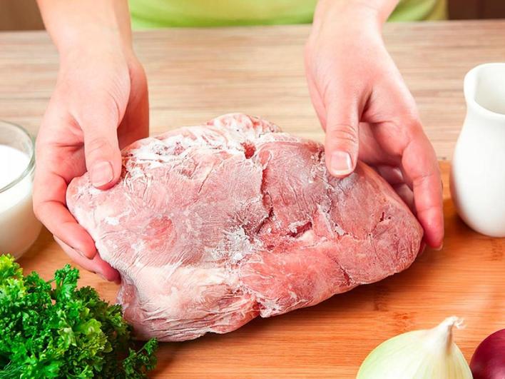 Una mujer deposita sobre una mesa de cocina una pieza de carne congelada.