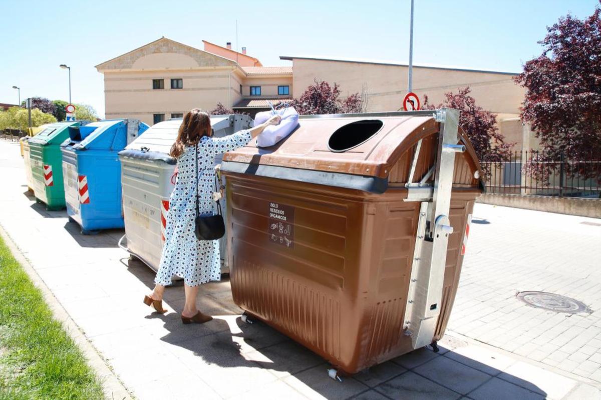 Una mujer deposita una bolsa en un contenedor marrón