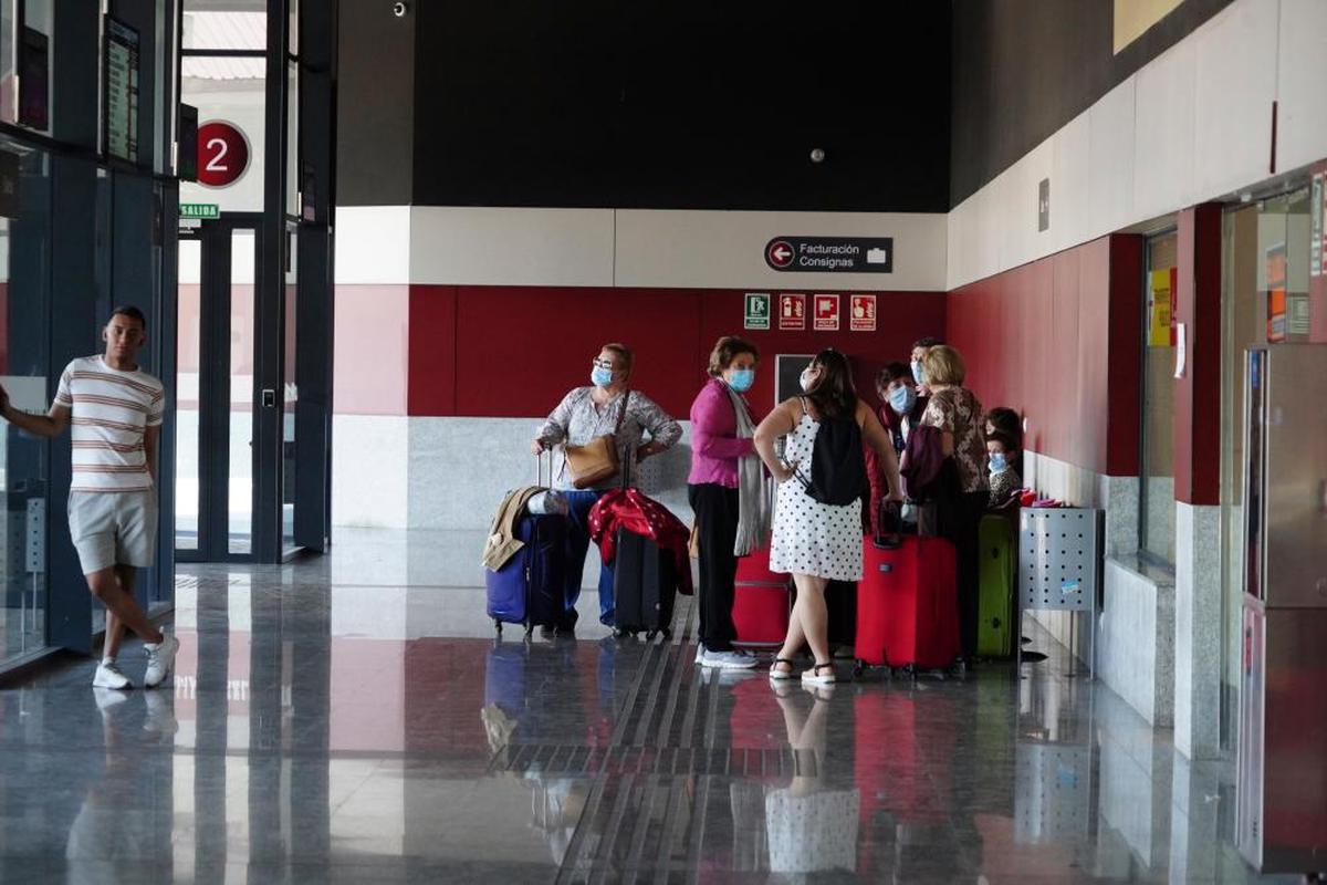 Varias personas esperan, junto a su equipaje, en la estación de autobuses para emprender sus vacaciones de verano.