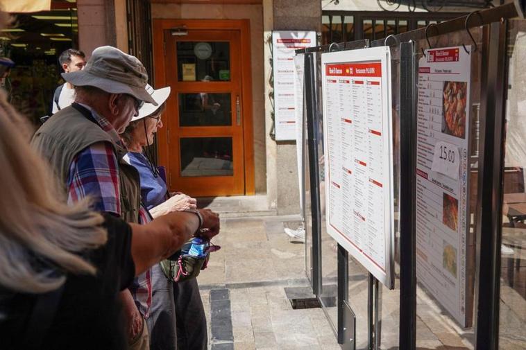 Turistas extranjeros echan un vistazo al cartel con la carta de un restaurante de la Rúa Mayor.