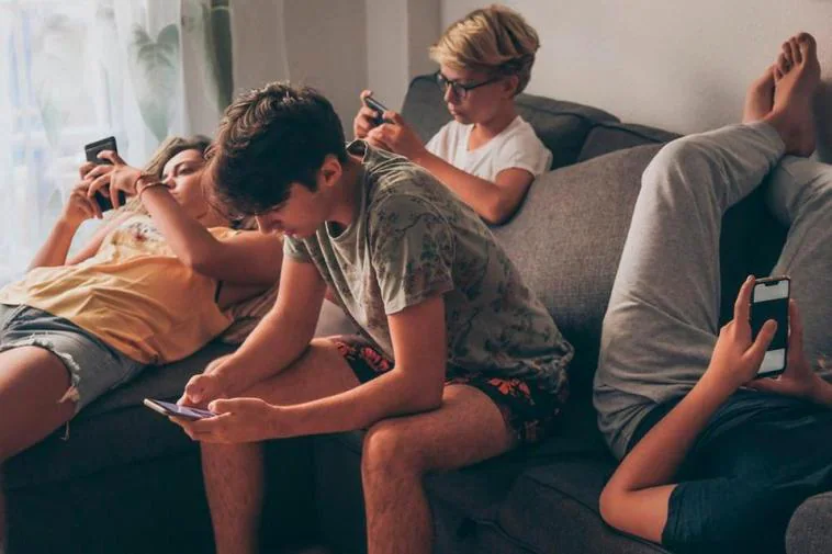 Grupo de adolescentes sentados mirando sus móviles.