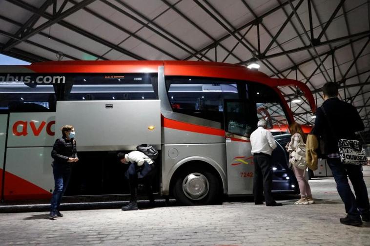 Dos viajeros esperando para subir al autobús en la estación. ALMEIDA