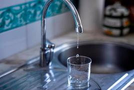 Un vaso de cristal coge gotas de agua de un grifo.