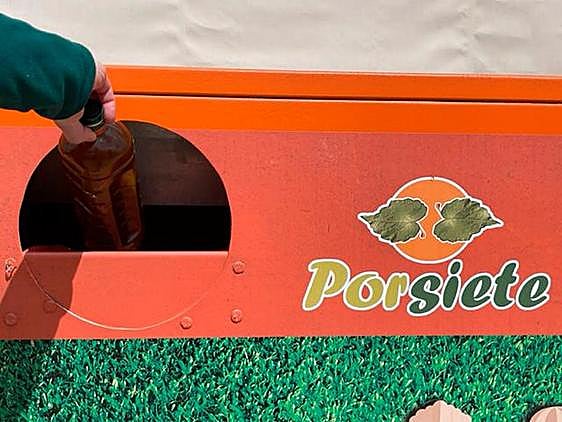 Una persona deposita una botella con aceite usado en un contenedor naranja