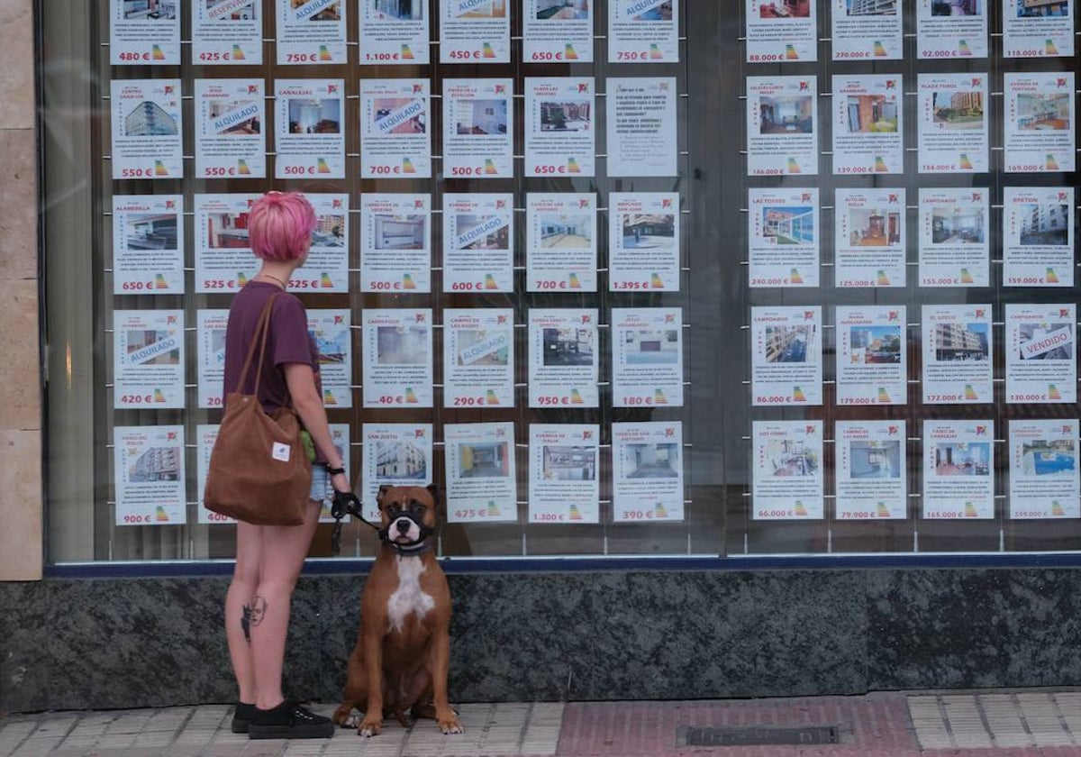 Una joven mira el escaparate de una inmobiliaria.