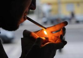 Un joven enciende un cigarrillo en la calle.