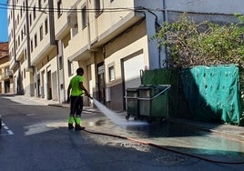 Imagen de un operario de limpieza retirando con agua la suciedad acumulada en ese tramo del acerado.