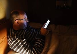 Un salmantino consulta su teléfono móvil desde la cama.