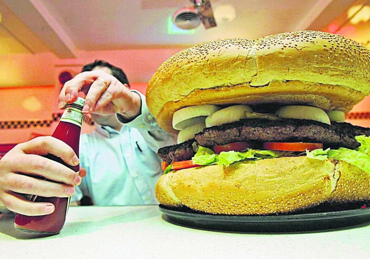 Un hombre se dispone a comer una hamburguesa en un local de comida rápida.