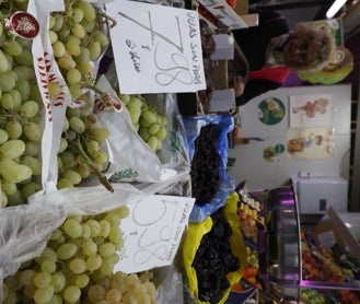 Imagen secundaria 2 - La frutera Susana Sánchez atiende a un cliente en su puesto en el mercado central. Los precios de las uvas con y sin pepitas.