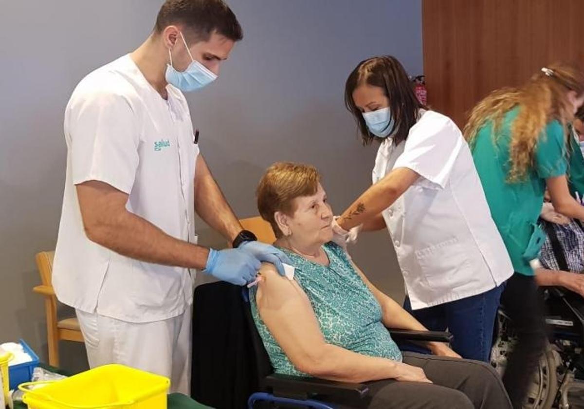 Dos sanitarios colocan una vacuna de la gripe a una persona mayor.