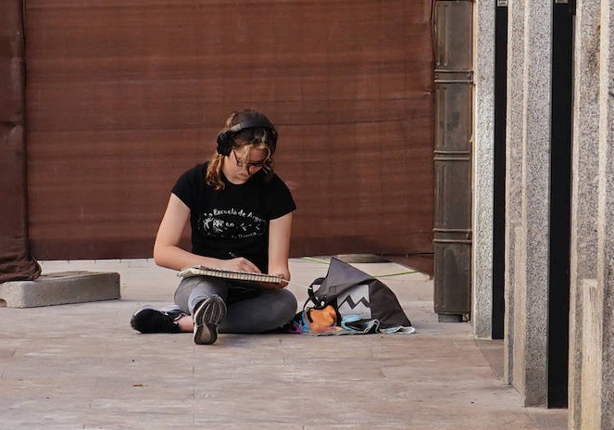 Una joven escucha con auriculares mientras que dibuja en Salamanca.