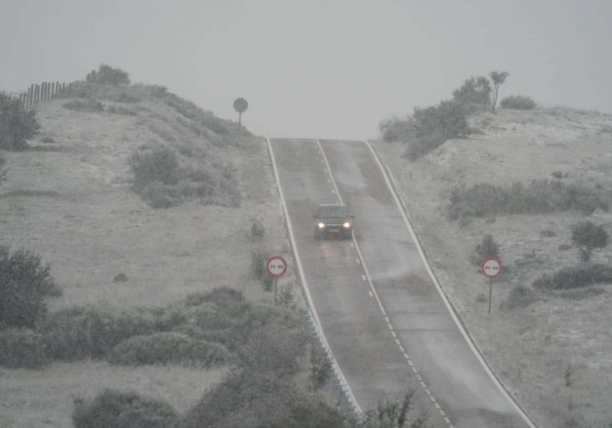 Un coche circula por la carretera durante este sábado bajo una intensa nevada.