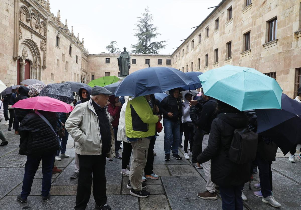 Viandantes se protegen de la lluvia con el paraguas frente a la fachada de la Universidad