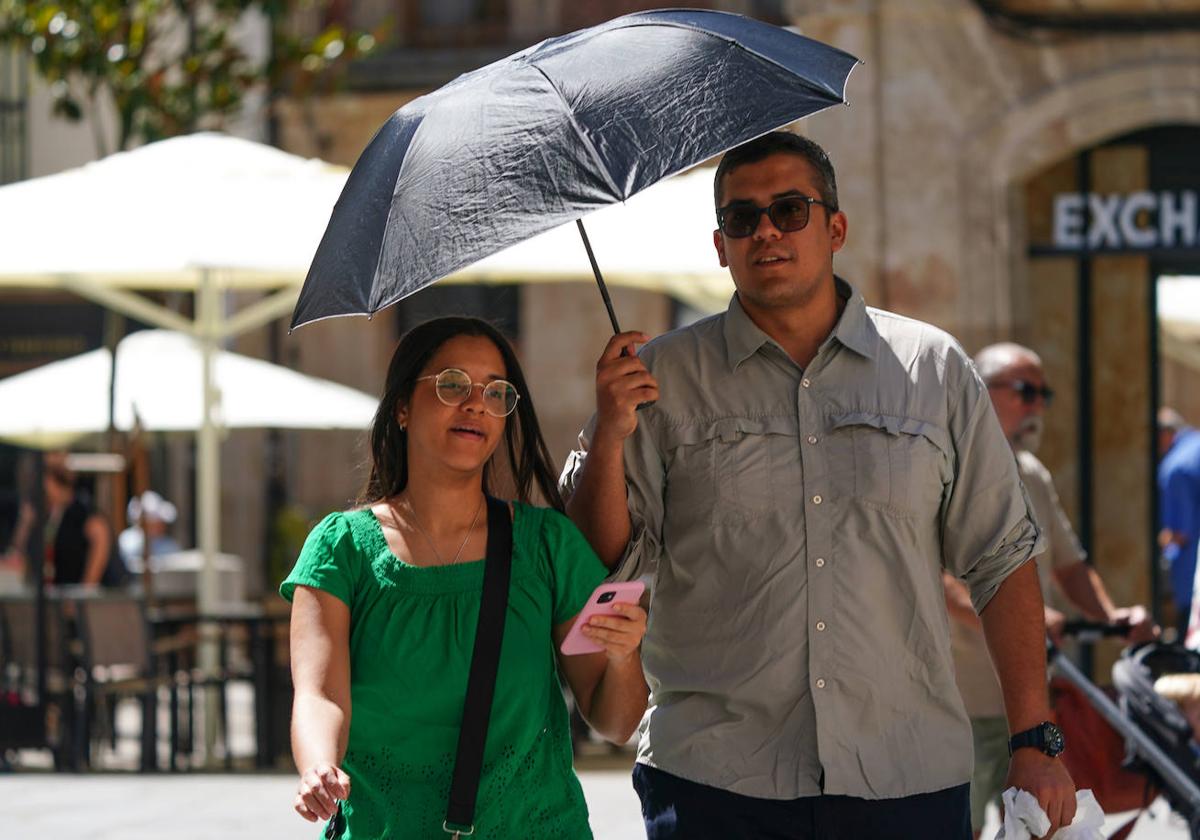 Una pareja se protege del sol con un paraguas mientras pasea por el centro de Salamanca.