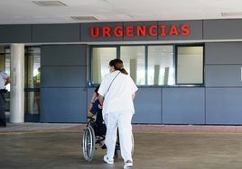 Una celadora empuja a un paciente en silla de ruedas en Urgencias.