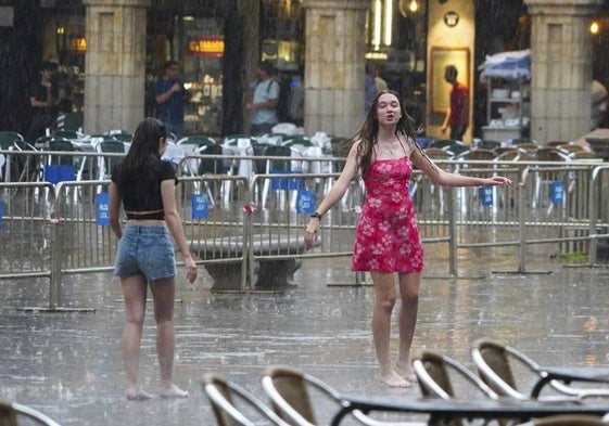 Dos chicas bailan en la Plaza Mayor bajo la lluvia.