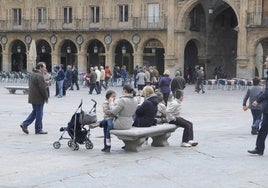 Una familia sentada en un banco de la Plaza Mayor en un día nublado.