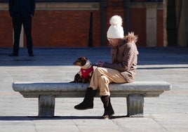 Mujer bien abrigada sentada en un banco junto a su perro.