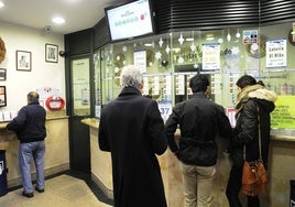 Varias personas hacen cola en una administración de lotería para coger un décimo de cara a la Lotería del Niño.