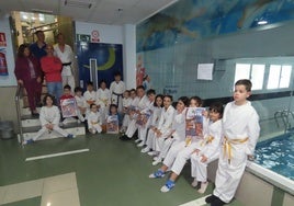 Alumnos del club de kárate posan con el cartel del evento.